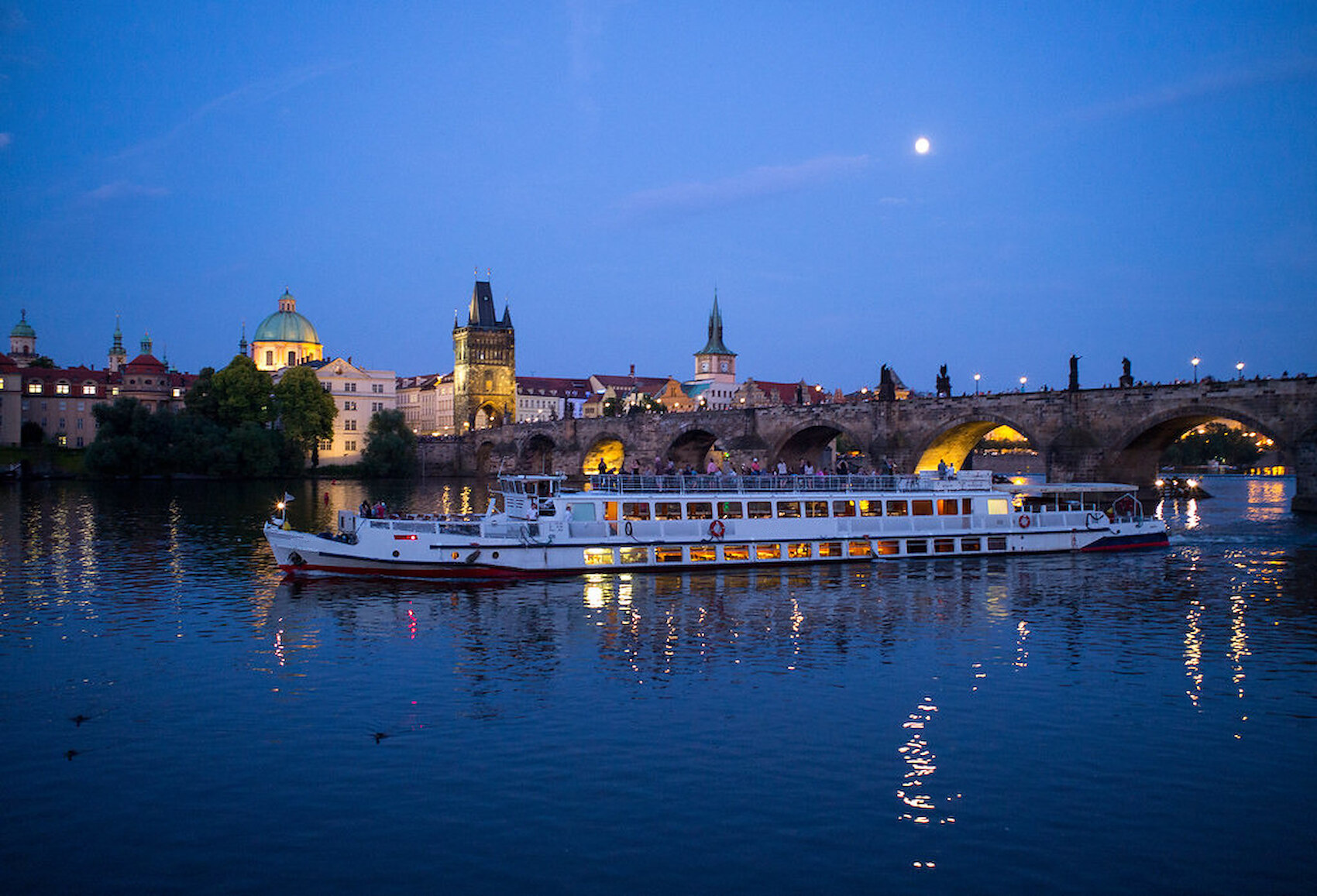 An illuminated sightseeing boat on the Vltava at dusk